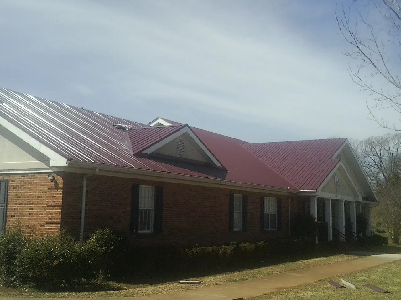 Red metal roof with gabled entries on a long brick building, from a Hail Damage Roof Repair job in Joppa