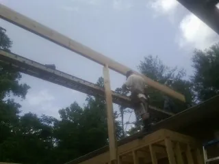 Carpenter setting a ridge beam over a new addition frame in Joppa